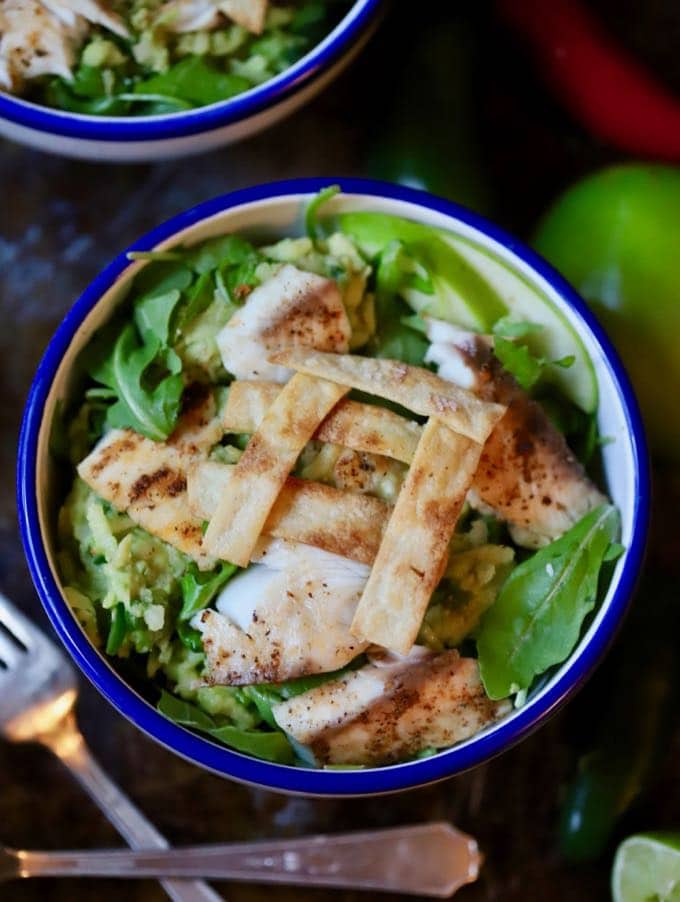 Fish Taco Bowl with Green Apple Guacamole on a bed of arugula topped with corn tortilla strips in a bowl.