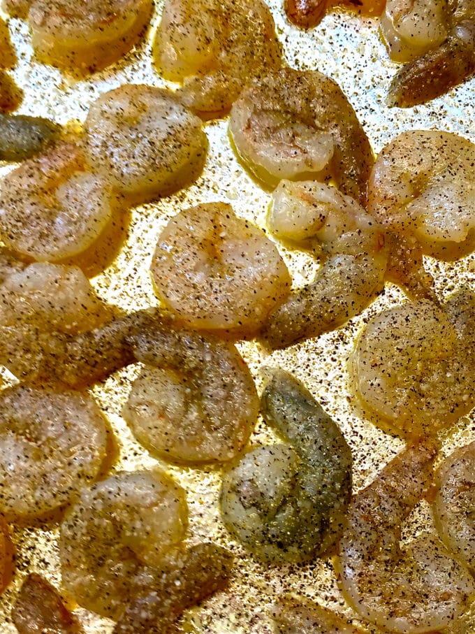 Raw shrimp on a baking sheet seasoned with salt and pepper. 