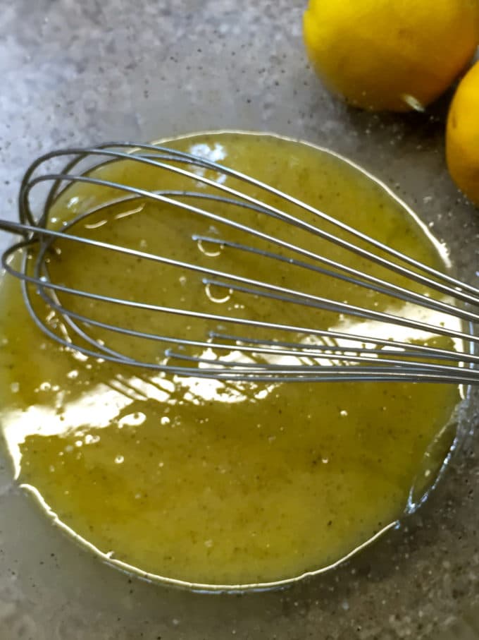 Lemon juice, olive oil and seasonings in a clear glass bowl to make a lemon vinaigrette. . 