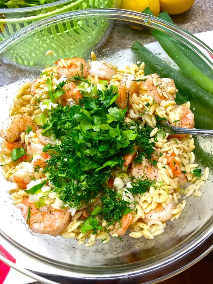A large glass bowl with orzo, shrimp and herbs ready to combine for shrimp pasta salad. 