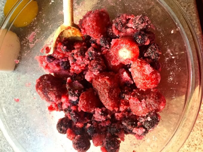 Frozen mixed berries in a clear glass bowl mixed with sugar.