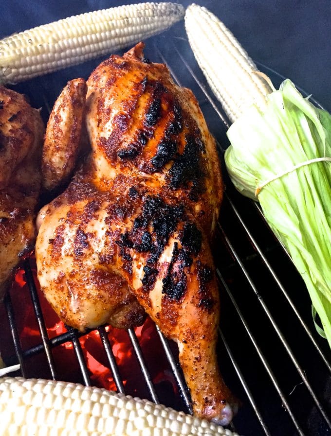 Half of a chicken grilling on a grill between two cobs of corn.