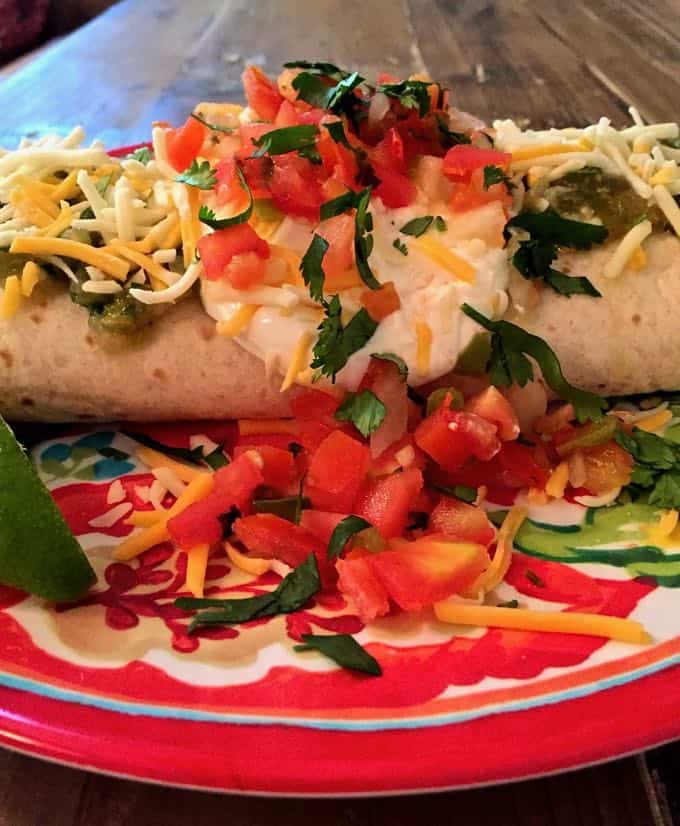 Salsa verde chicken enchiladas on a multi-colored plate topped with sour cream, tomatoes and cheese.