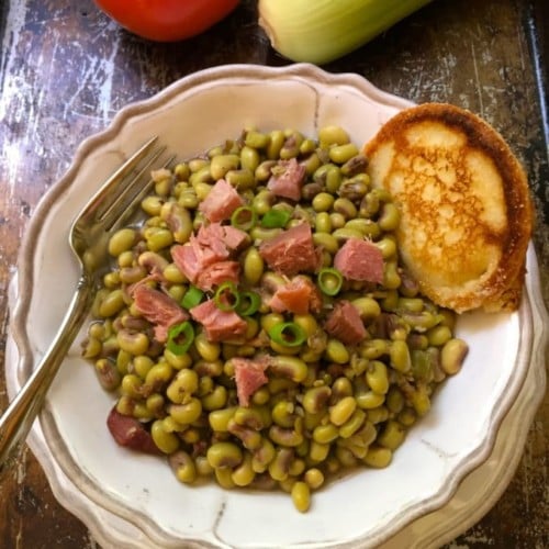 Southern Pink Lady Peas in a white bowl topped with chunks of ham and a hoecake