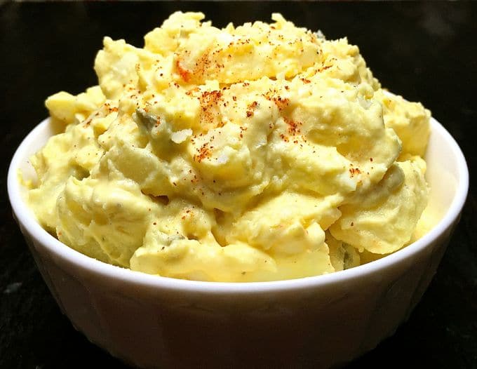 A white bowl full of potato salad topped with paprika. 