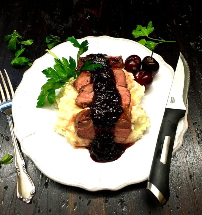Grilled Pork Tenderloin with Dark Cherry Sauce on a white plate on top of mashed potatoes