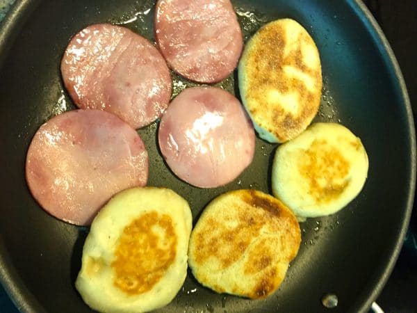 Four English muffins and four ham slices in a large skillet.