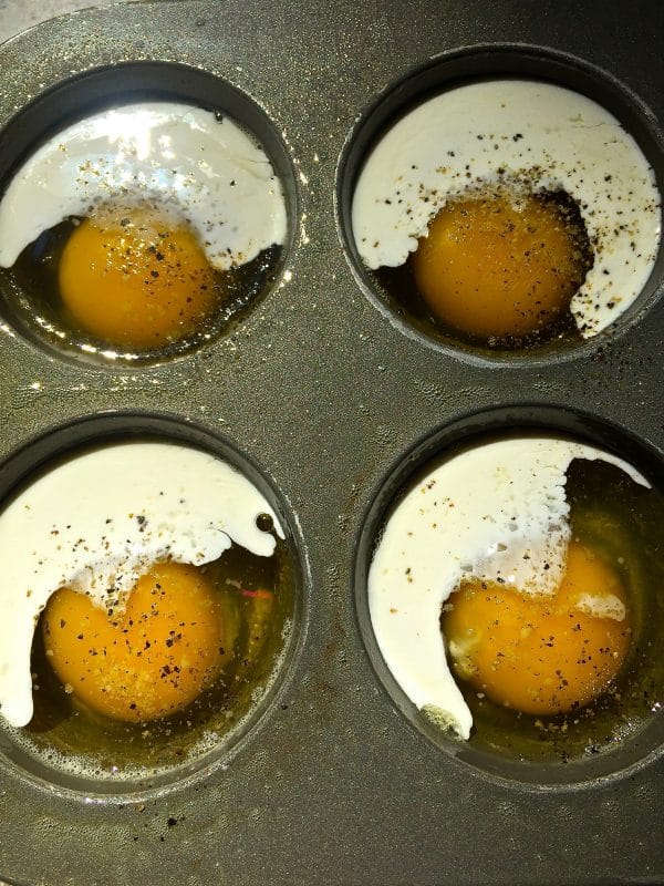 Four eggs in a muffin pan with cream, salt and pepper.