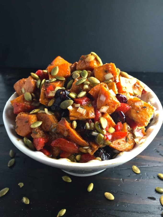  Roasted Sweet Potato Salad topped with toasted pumpkin seeds in a white bowl.