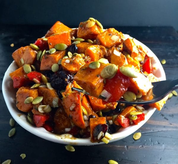  Roasted Sweet Potato Salad topped with toasted pumpkin seeds in a white bowl with a fork full.