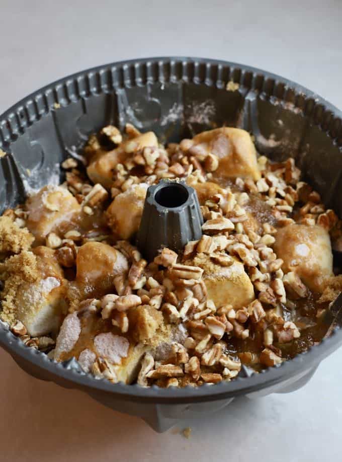 Brown sugar and pecans top frozen bread roll dough in a bundt pan.