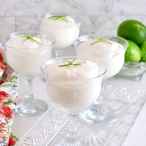 Four key lime mousses garnished with a lime wedge in parfait glasses.