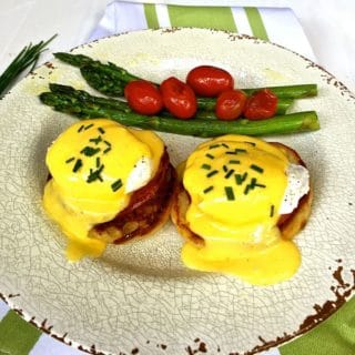 Eggs Benedict garnished with chives and asparagus and cherry tomatoes on the side.