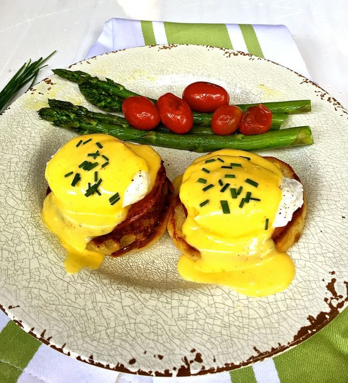 Eggs Benedict garnished with chives and asparagus and cherry tomatoes on the side.