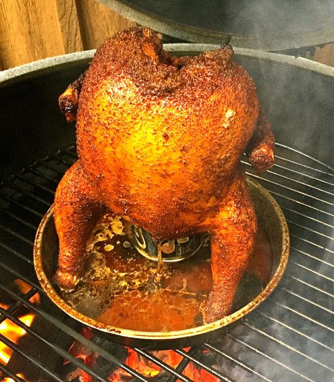 A whole chicken sitting on a can inside of a pie plate on the grill cooking.