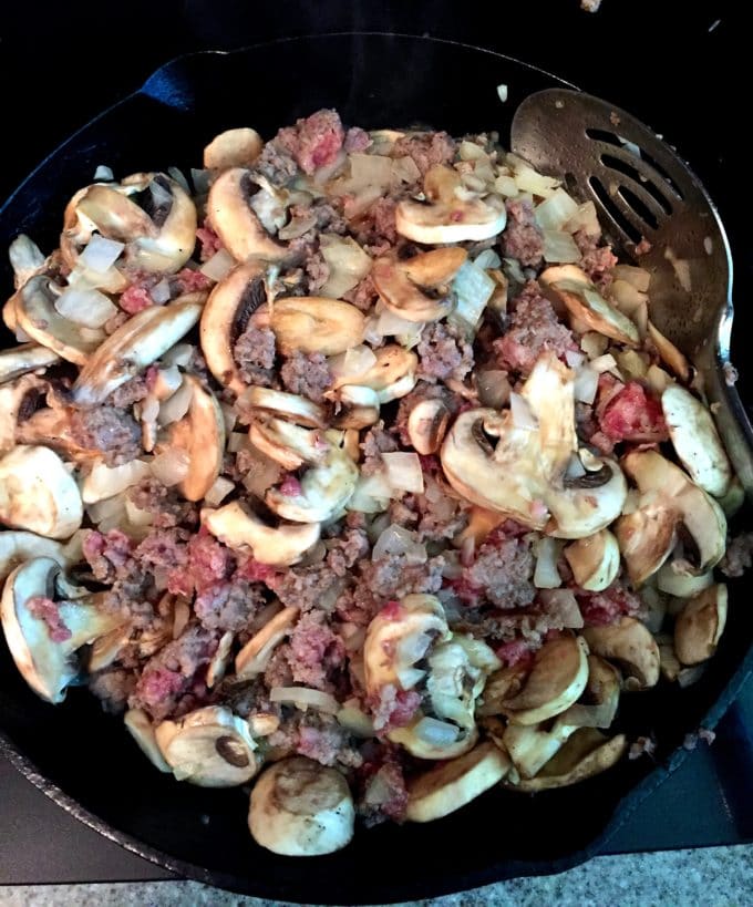 Cooking sausage, mushrooms, and onions in a skillet. 