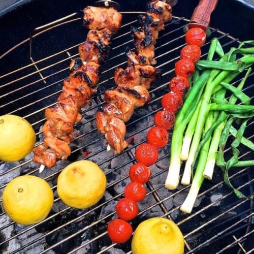 Grilled Chicken Skewers, cherry tomato skewer, scallions and lemons on a grill.