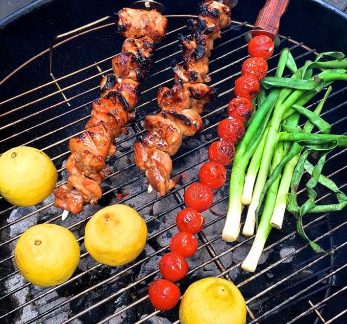 Grilled Chicken Skewers, cherry tomato skewer, scallions and lemons on a grill.