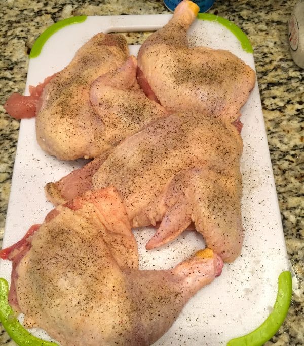 Four bone-in chicken pieces sprinkled with salt and pepper on a cutting board.