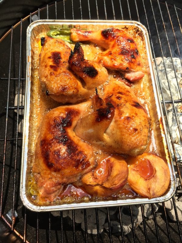 Chicken pieces in the pan with peach halves and jalapeño halves on the grill rotated.