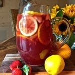 Sangria in a glass pitcher with orange and lemon slices and strawberries