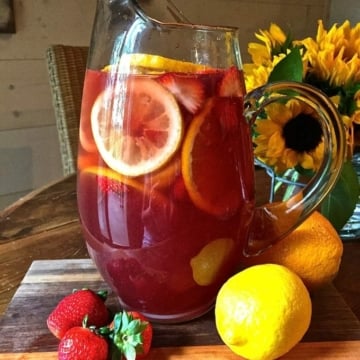 Sangria in a glass pitcher with orange and lemon slices and strawberries