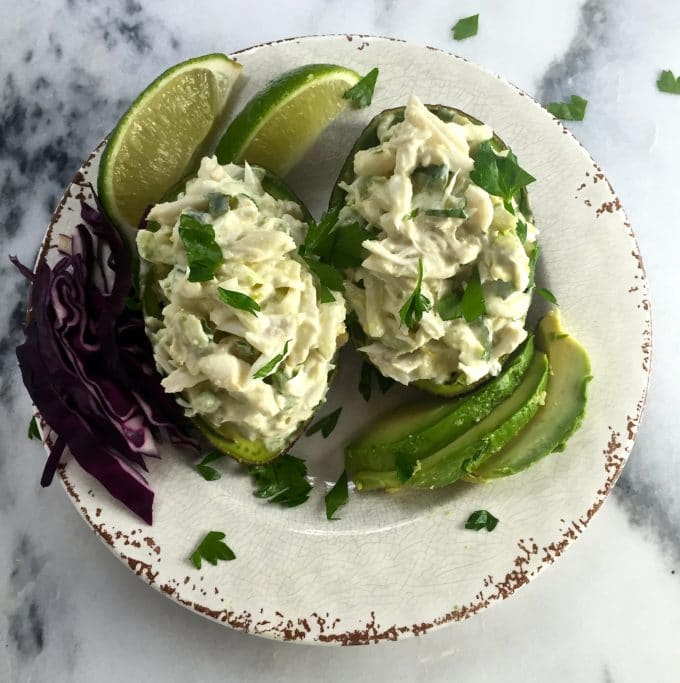 A plate with two avocados stuffed with a blue crab mixture garnished with lime slices.