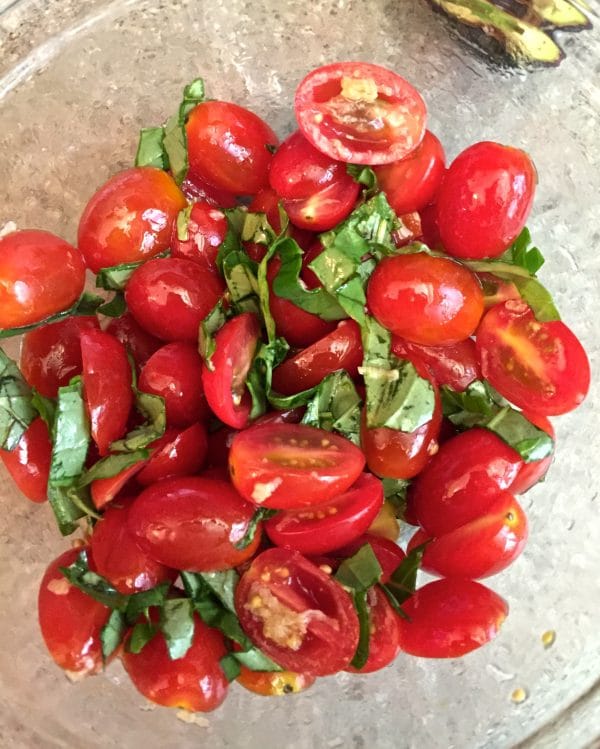 Sliced tomato halves and basil in a medium sized glass bowl.