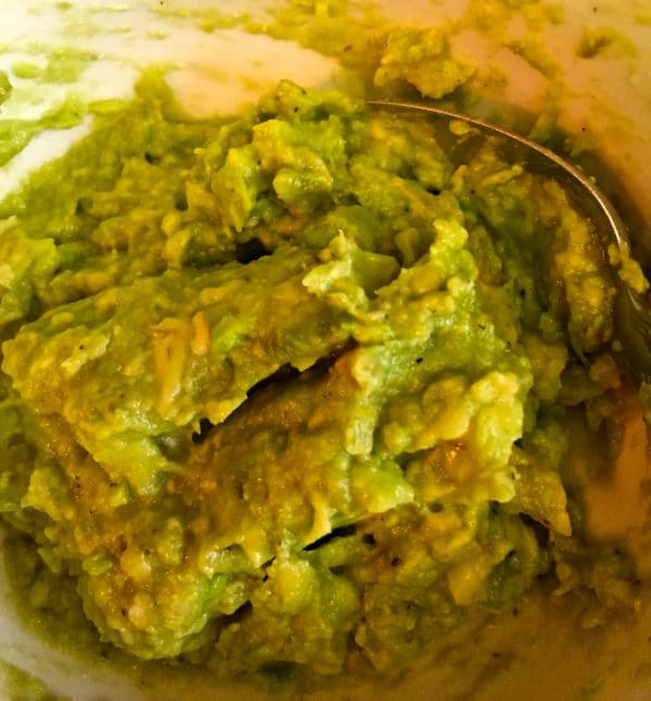 Mashed avocados in a medium size bowl with a spoon.