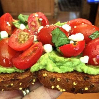 Bruschetta Avocado Toast with crumbled goat cheese and fresh basil for garnish.