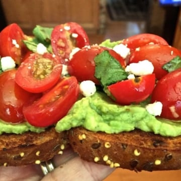 Bruschetta Avocado Toast with crumbled goat cheese and fresh basil for garnish.