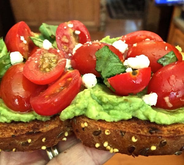 Bruschetta Avocado Toast with crumbled goat cheese and fresh basil for garnish.