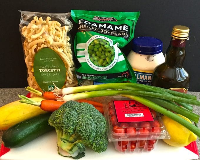 A bag of pasta, edamame, broccoli, carrots, scallions and cherry tomatoes.