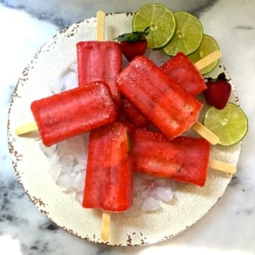 Strawberry Margarita Ice Pops on a white plate with ice, lime slices and strawberries