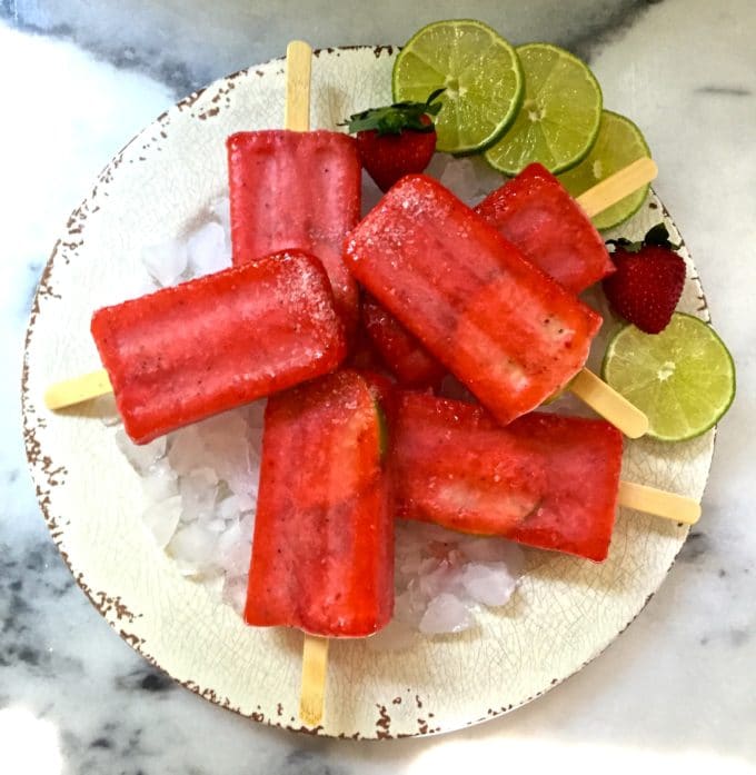 Strawberry Margarita Ice Pops on ice garnished with lime slices and strawberries