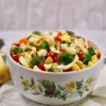 A large bowl with pasta salad and vegetables on a white and green napkin.