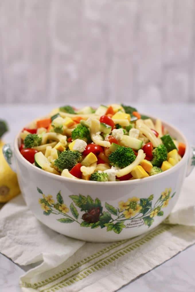 A large bowl with pasta salad and vegetables on a white and green napkin.