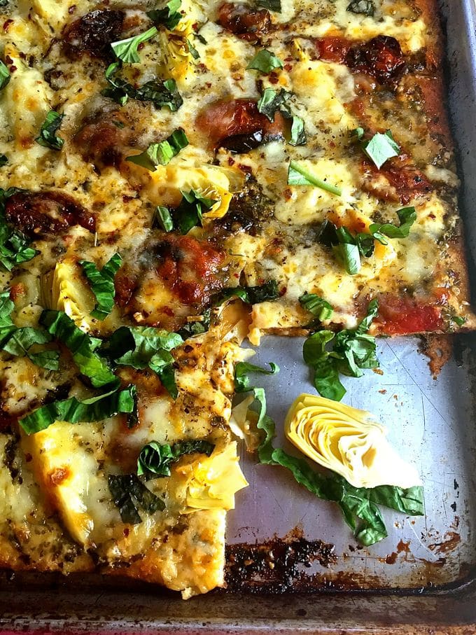 Tomato and Artichoke Pizza garnished with basil missing a slice on a baking sheet.
