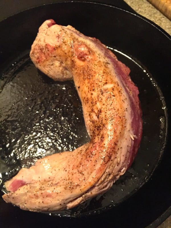 Pork tenderloin sprinkled with salt and pepper in a cast iron skillet.