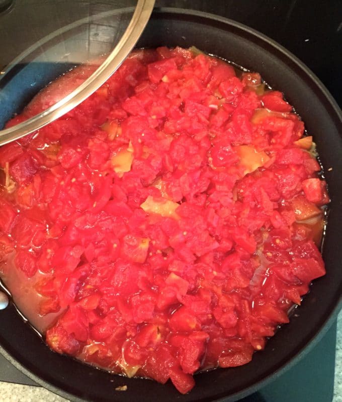 Diced tomatoes, pieces of lasagna noodles and sausage cooking in a skillet.