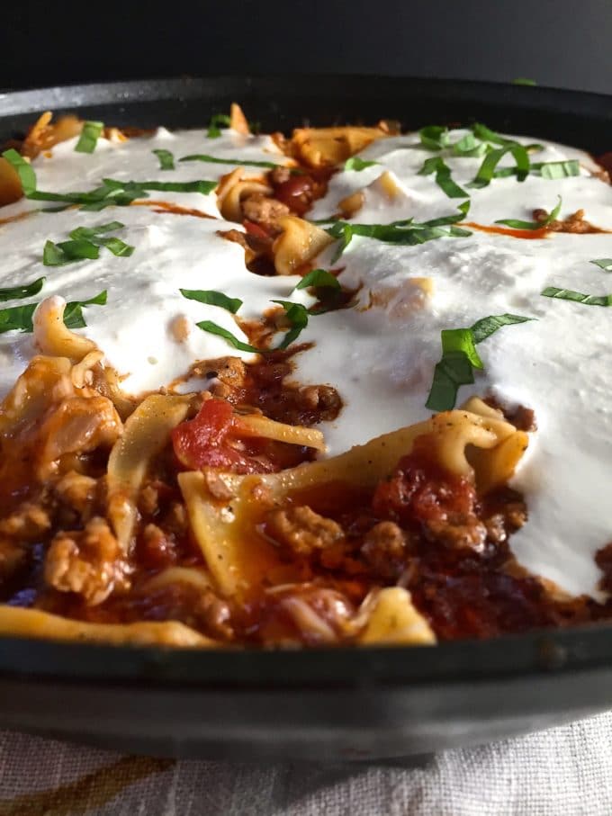 Skillet lasagna topped with melted ricotta cheese cooks in a skillet.