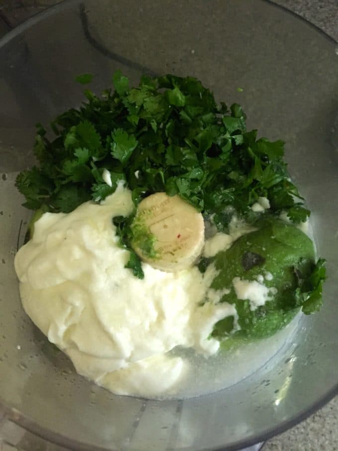 Sour cream, avocado, and cilantro in the bowl of a food processor.