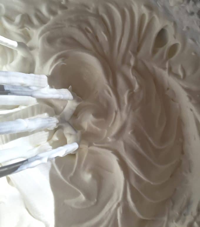 Sugar and heavy cream mixing with an electric mixer in a large mixing bowl.