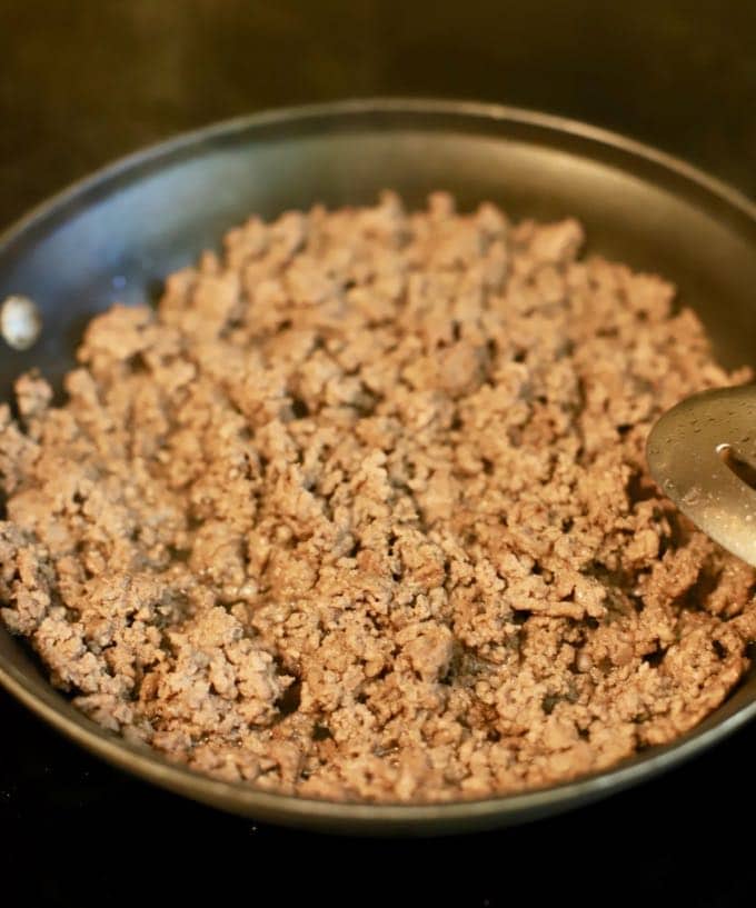 Ground beef browning in a skillet on the stove.