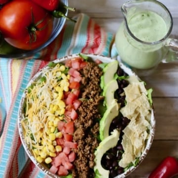 Taco salad in a large bowl next to a pitcher of avocado dressing.
