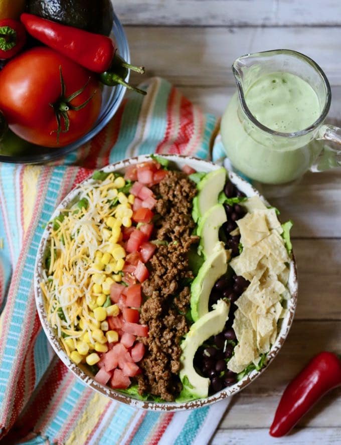 A large taco salad in a bowl on a brightly striped Mexican towel.