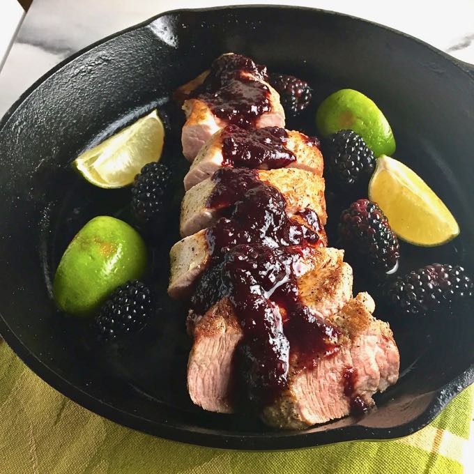 Pork Tenderloin with Blackberry Sauce in a cast iron skillet with blackberries and lime wedges.