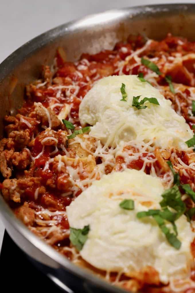 Skillet lasagna topped with ricotta and mozzarella cheeses in a skillet.