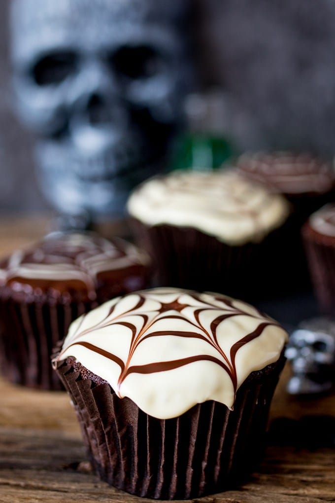 Chocolate Halloween Spider Web Cupcakes with white icing and a spider web drawn on the top.
