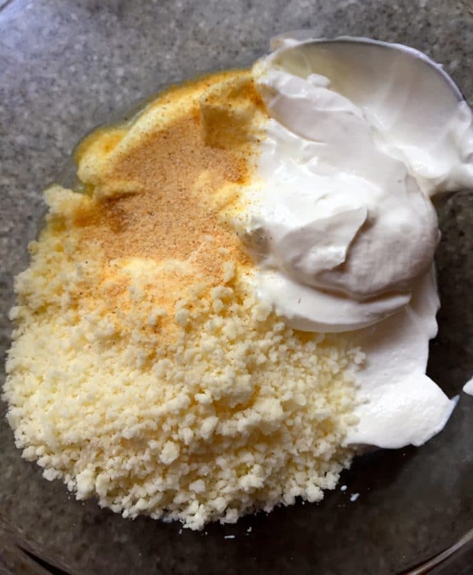 Sour cream, grated parmesan cheese, and onion powder in a clear glass bowl.